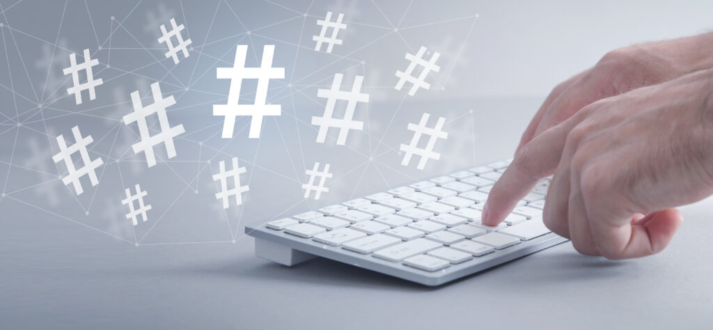 This is an image of two hands typing on a keyboard and from that keyboard some hashtags are coming out and flying into the air.