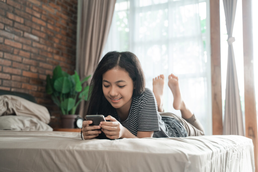 This is an image of a girl laying on her stomach looking at her phone.