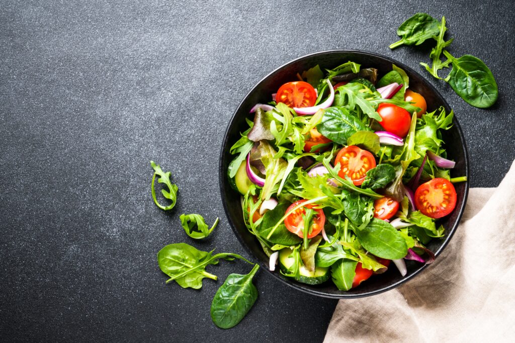 Salad in a bowl sitting on a table. The salad has lettuce and tomatoes in it.