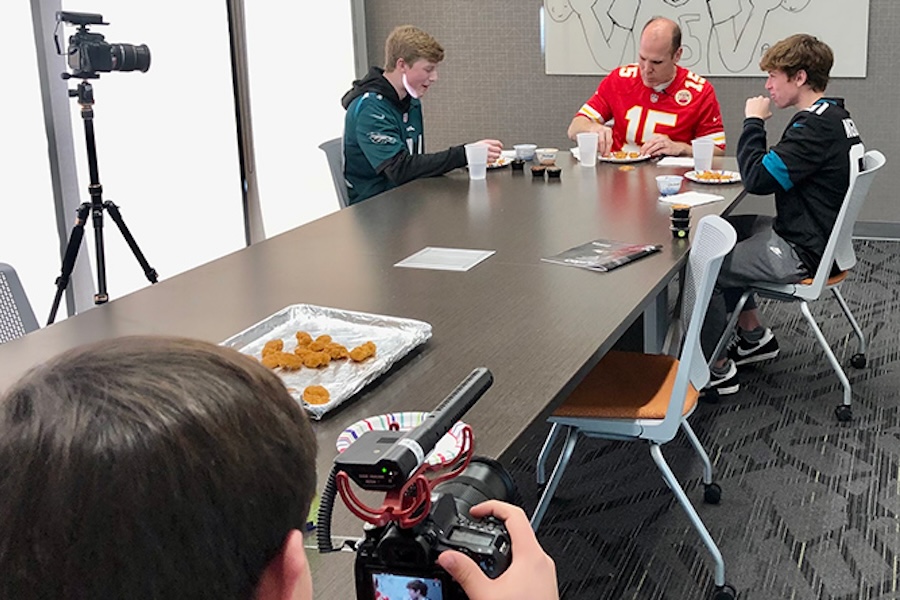 Photo of someone recording a video of 3 people eating
