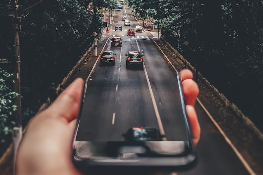 Questions_Aug23 Photo of a person holding a phone with an image of a road who is standing over a road with cards and the roads line up
