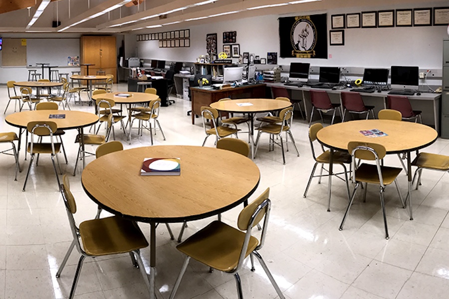 Photo of an amazing looking classroom that features a flag, table and chairs, cool lighting and spectacular yearbooks and magazines.