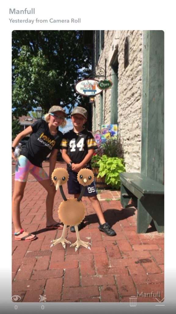 Photo of two kids who wear iowa Hawkeyes merch as they pose on main Street next to a Pokemon on the Pokemon Go app