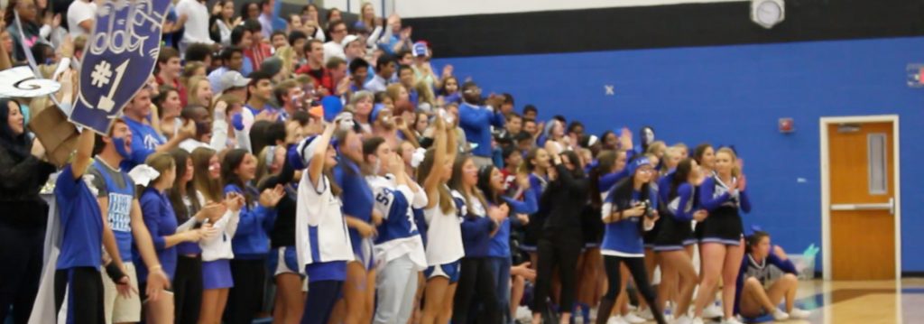 Photo of a high school pep rally with students and cheerleaders cheering from the stands