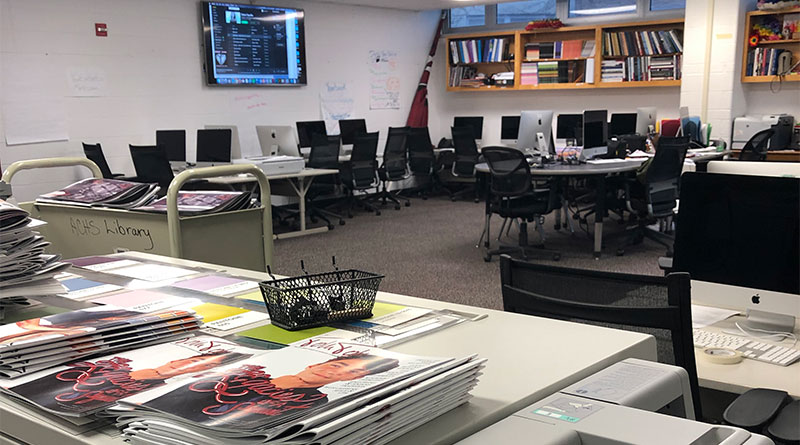 Photo of a newsroom with magazines, and lots of computers and tables
