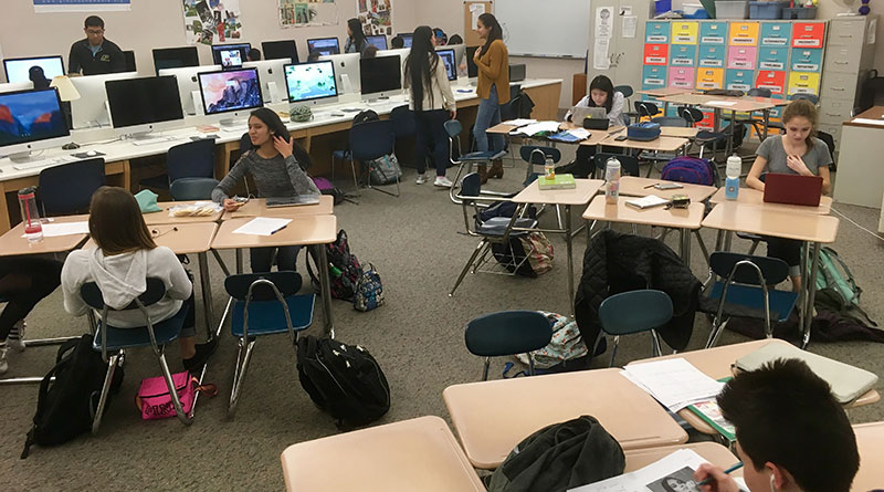 Photo of a newsroom with rows of tables ad computers with students at desks, a color coded filing cabinet lives against a wall
