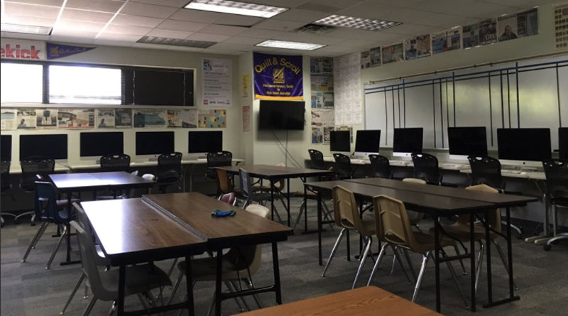 Photo of a newsroom that has tables and rows of computers and chairs. A quill and Scroll banner also hangs on the wall