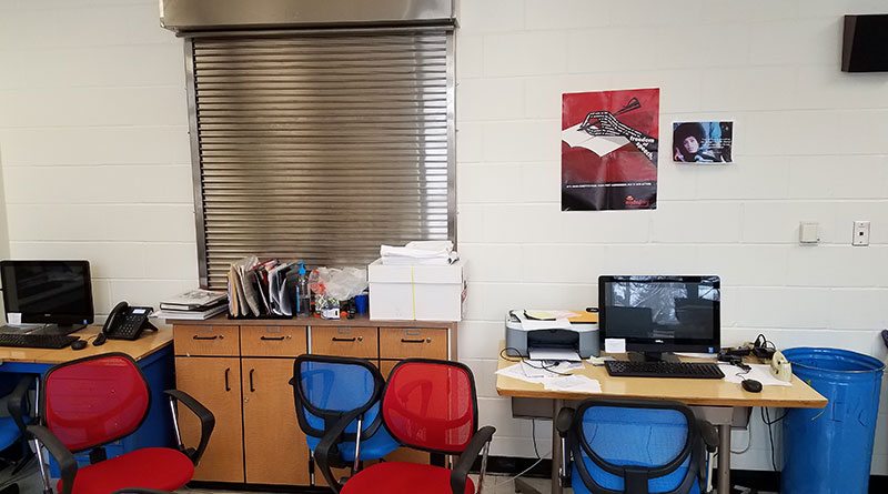 Photo of a newsroom that features blue and red chairs and computers at desks