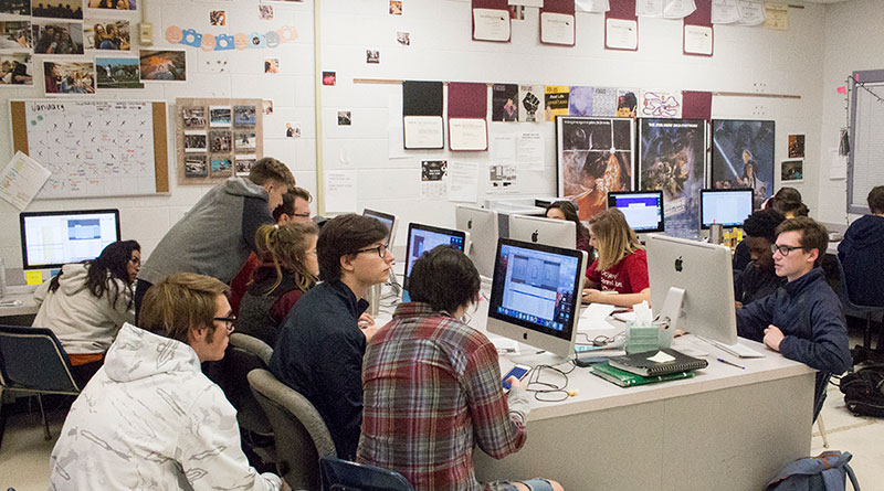 Photo of students working in a newsroom with many students working together