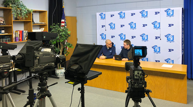 Photo of two people at a news desk being recorded for a news broadcast