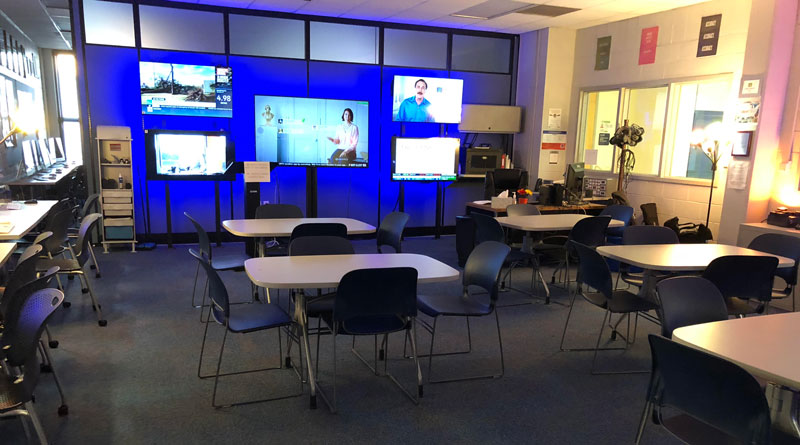 Photo of a newsroom with 5 TV's on turned to news stations and lots of desks and chairs