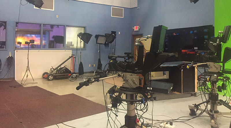 Photo of a news broadcast setup with cameras and a green screen