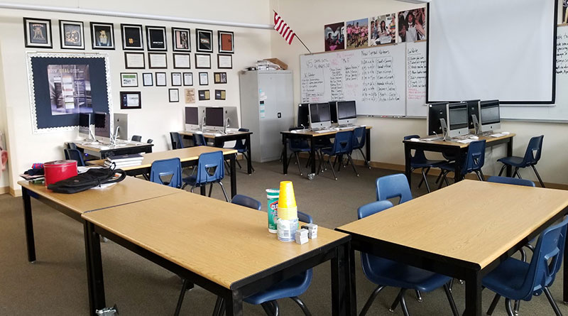 Photo of a newsroom that has desks of computers with a pull-down screen and writing on the whiteboard