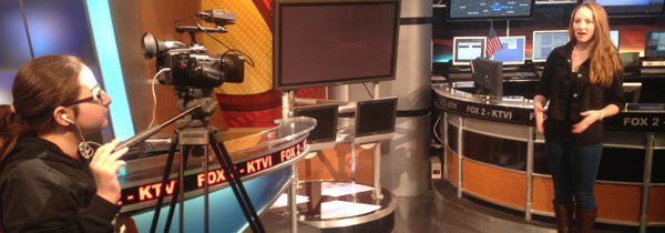 Photo of a girl giving a news broadcast while being recorded by a girl