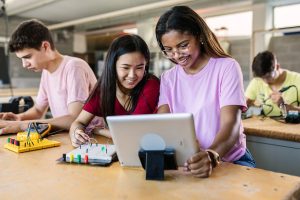 Photo of two girls using a iPad and engineering equipment and other students using technology
