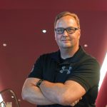 Jeff Doles stands with his arms crossed, smiling in front of a red wall