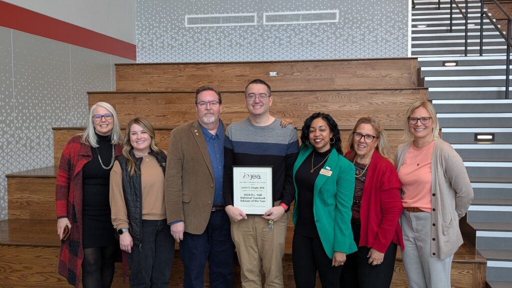 Justin Daigle poses with his Yearbook Adviser of the Year award and the JEA team that surprised him with it.