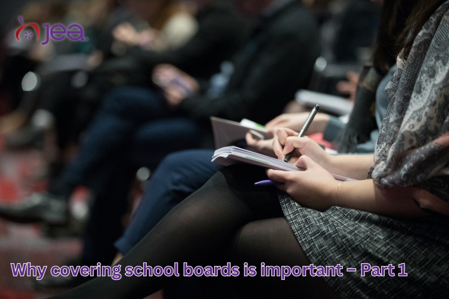 Image of reporters sitting. Those in the foreground are holding a reporter's notebook and writing utensils. The image contains the JEA logo in the upper left corner and the text "Why covering school boards is important – Part 1."