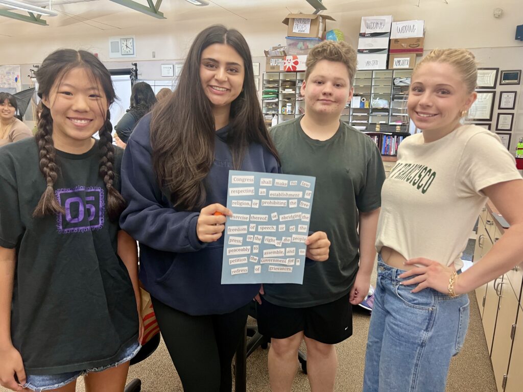 Image contains four high school students holding up a sign with cutout words on blue poster paper.