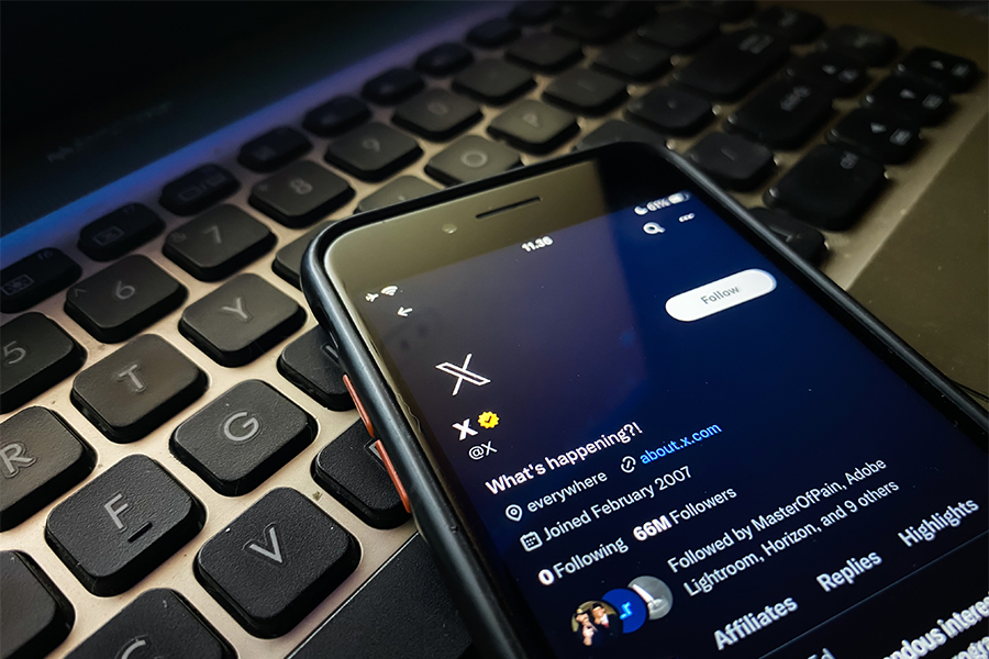 This is a computer keyboard with phone on top if it. One the phone is a visual of a social media feed from x.