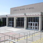 Photo shows the front of Lowell High School, a gray block building with entry doors and railings.