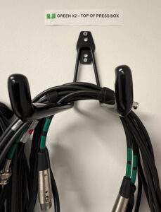 These are cables hanging from a bracket on a wall. The cables have two lines of green electrical tape near each end. 