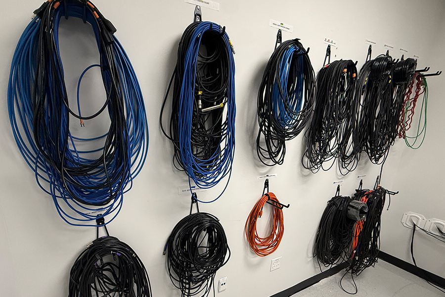 This is an image of a wall. On the wall there are brackets coming out from the wall and different types of cables are hanging from the brackets.